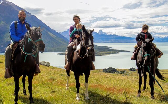 El Calafate – Familie beim Reiten in der patagonischen Steppe mit Blick auf den türkisfarbenen Lago Argentino und die umliegenden Berge.
